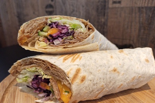 Dürüm Wrap mit Kebapfleisch, Salat, Rotkraut und Sauce, halb aufgeschnitten auf Holztisch angerichtet