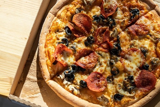 Frisch gebackene Pizza mit Salami, Käse und Gemüse in Kartonbox auf Holztisch